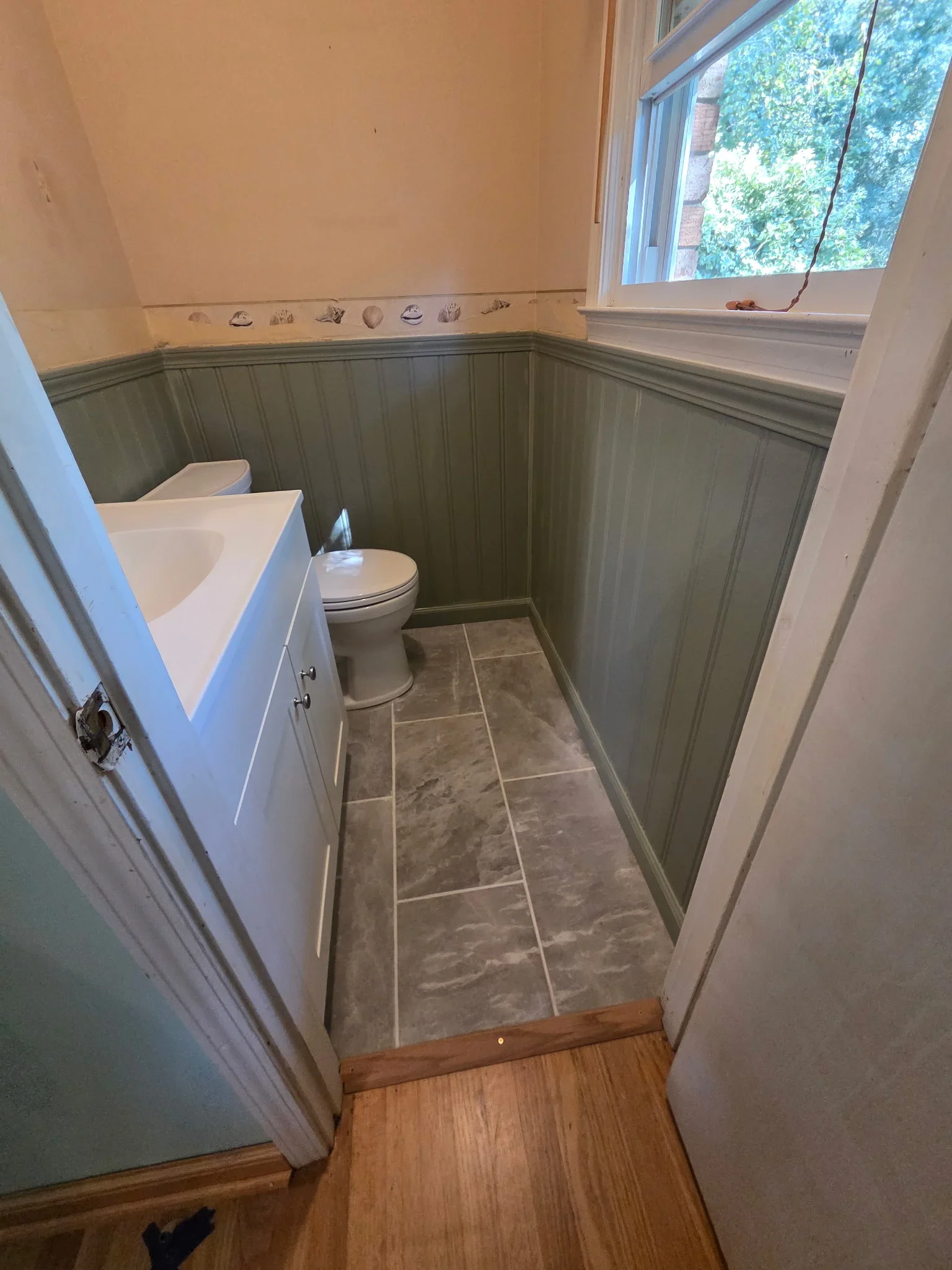 Powder room with sage green wainscoting, cream walls, gray tile floor, white vanity and toilet