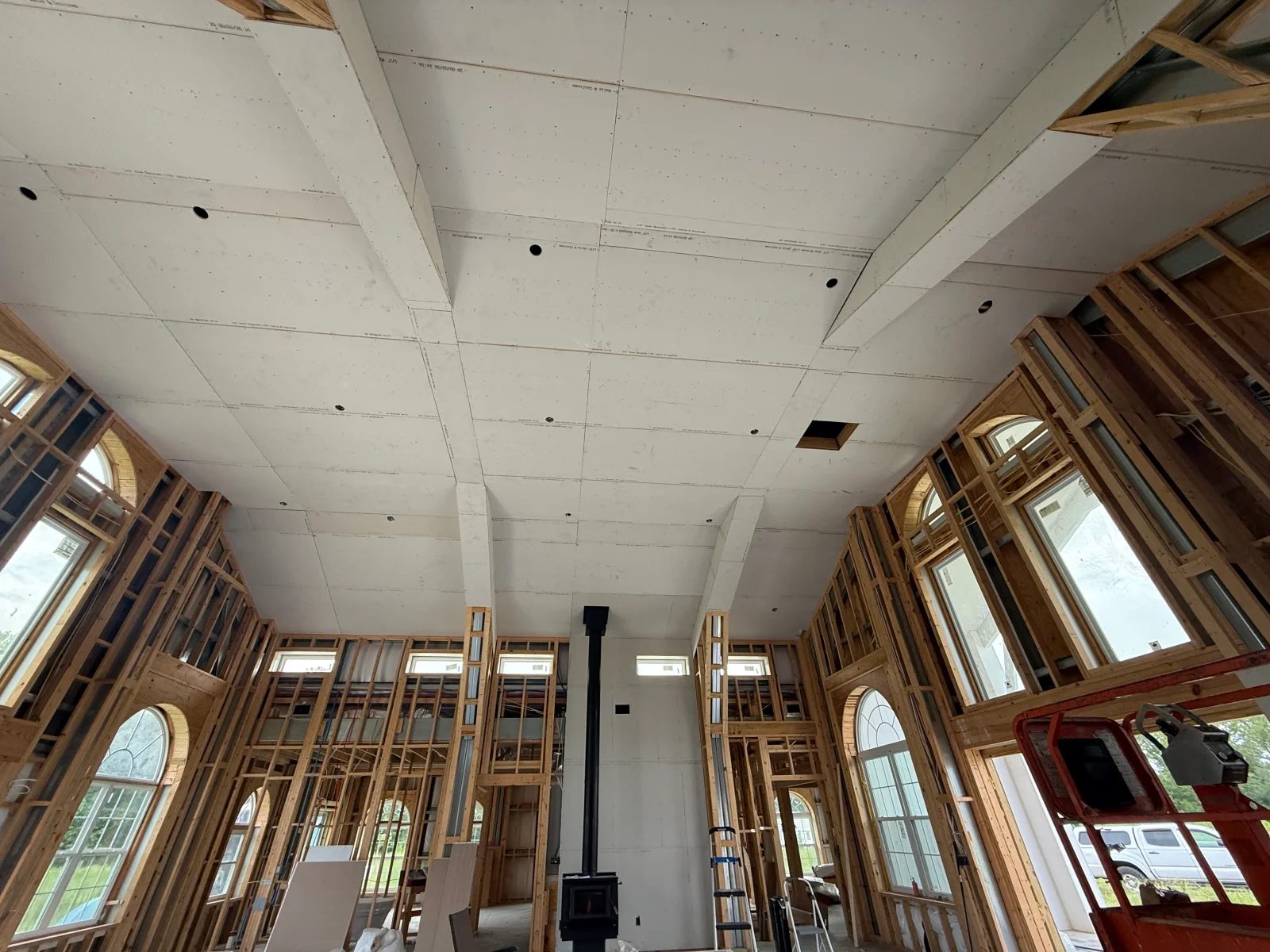 Vaulted ceiling drywall installation with recessed lights, wood framing, and window rough-ins