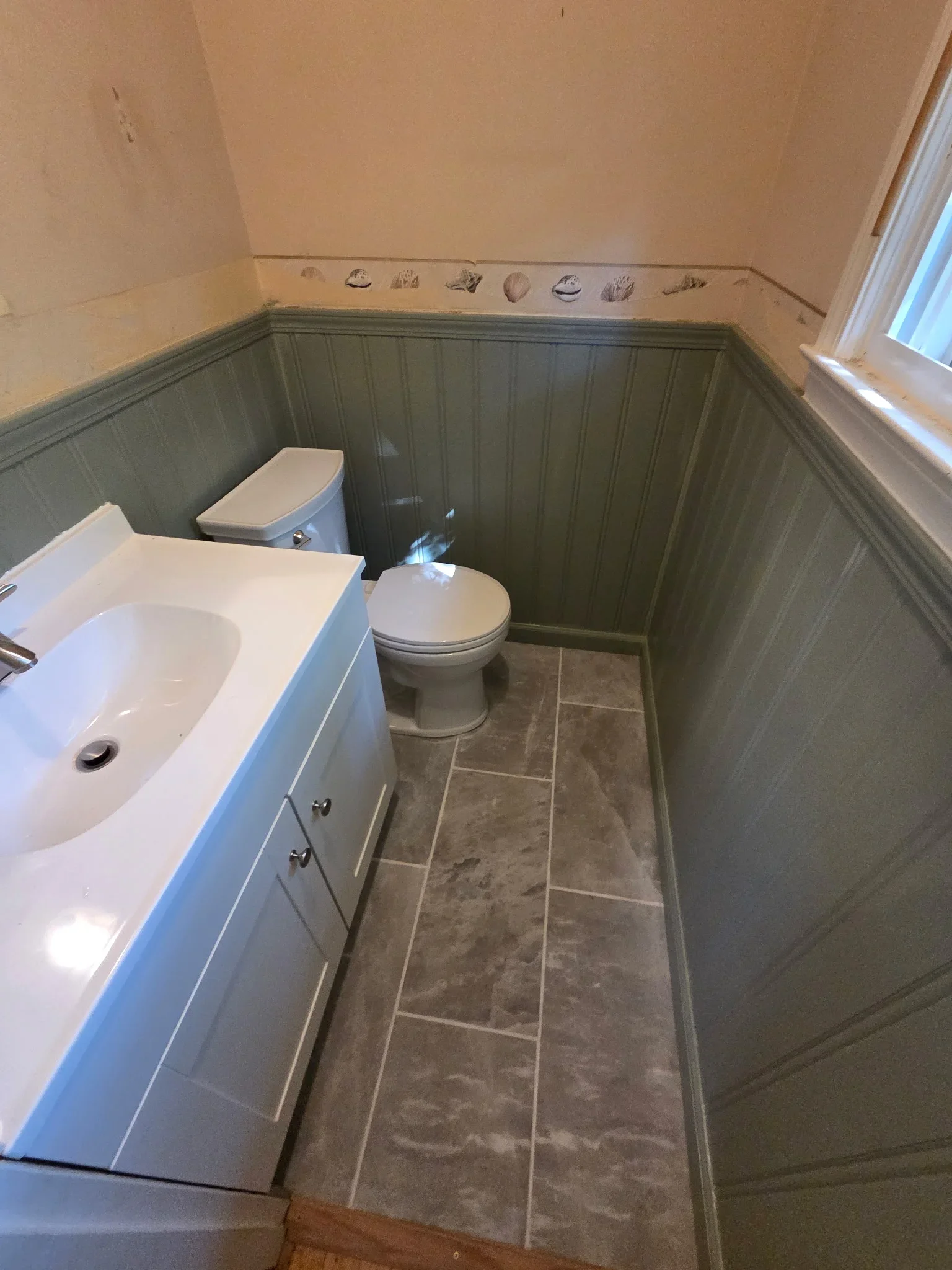 Bathroom with sage green wainscoting, stone-look tile floor, white vanity and toilet