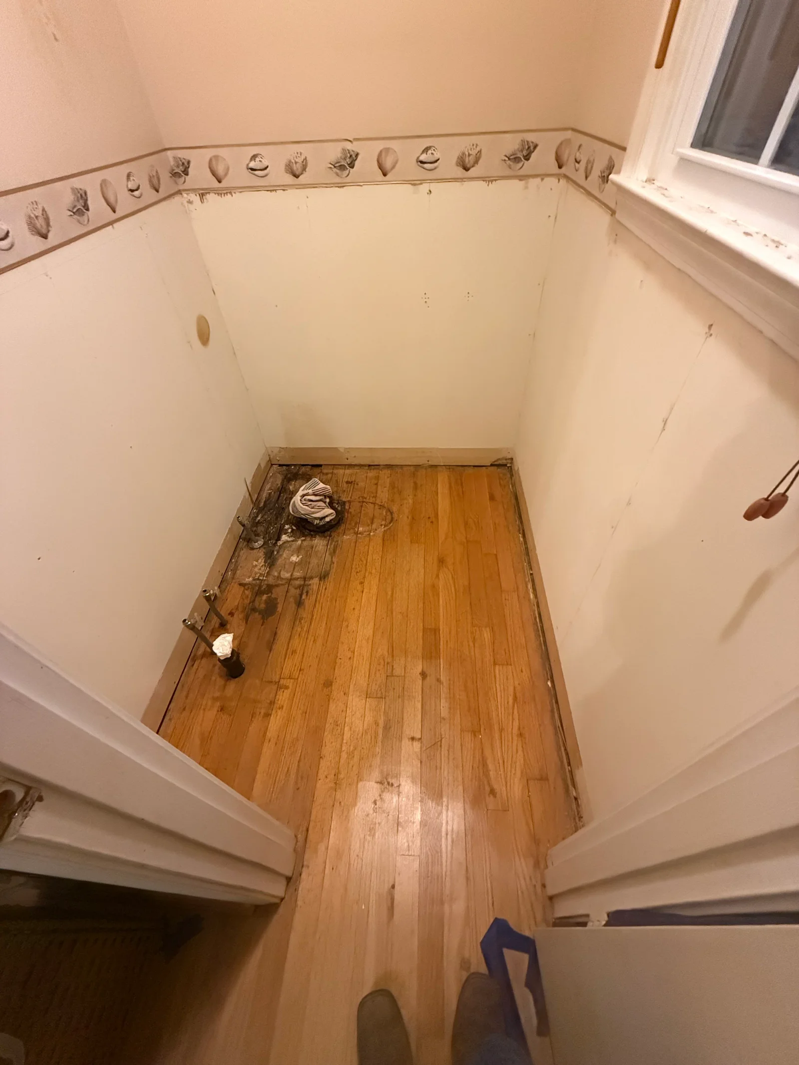 Bathroom interior with new drywall, decorative border trim, and original hardwood flooring during renovation