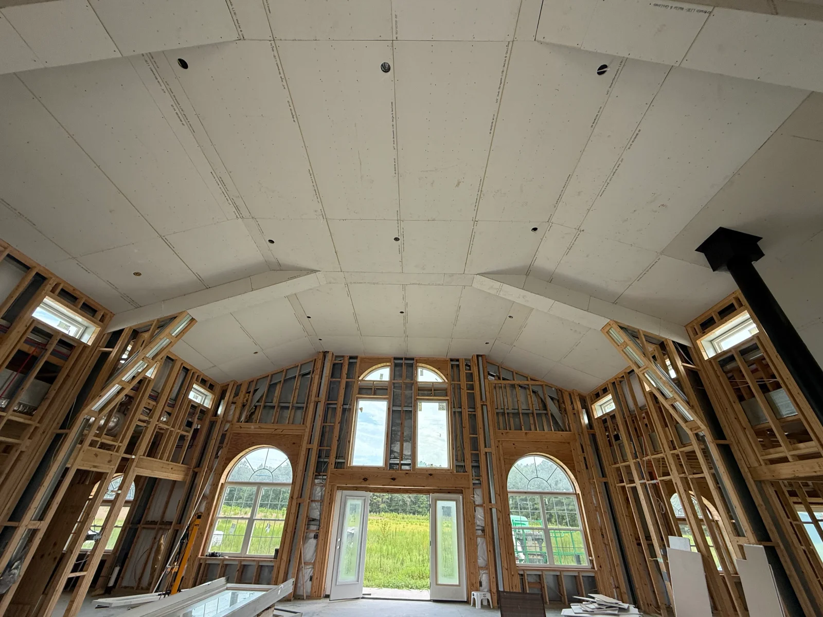 Vaulted ceiling drywall installation with wood framing, recessed lights, and arched window openings