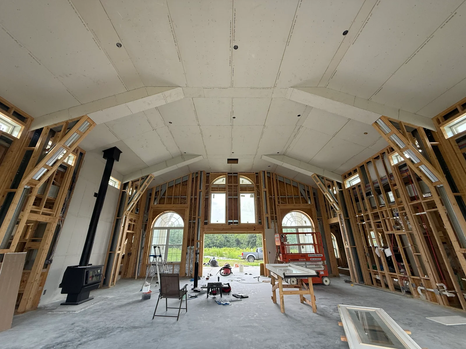 Vaulted ceiling drywall installation with wood framing, recessed lights, and transom windows in open-concept home interior