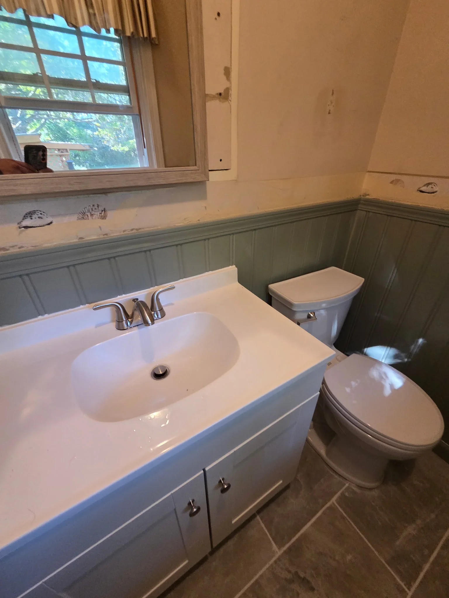 Bathroom with white vanity, dual toilets, sage wainscoting, and tile flooring